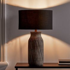 a lamp that is sitting on a table next to a book and a vase with a black shade