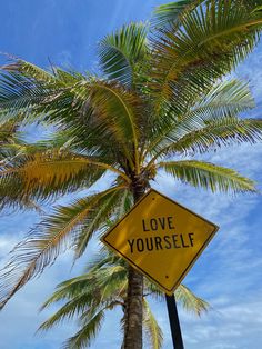 a yellow sign that says love yourself under a palm tree