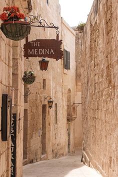 an alley way with stone buildings and flowers hanging from the ceiling, along with a sign that says the mediana