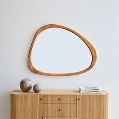 an oval wooden mirror on the wall above a dresser with two vases next to it