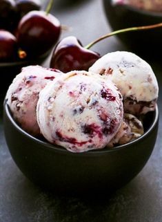 three scoops of ice cream in a bowl with cherries on the table behind them