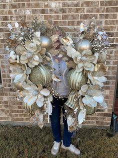 a woman standing in front of a brick wall holding a wreath made out of ornaments