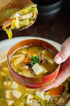 a hand holding a spoon full of soup with tofu and other foods in it