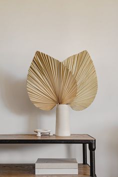 a white vase sitting on top of a wooden table next to a book and lamp