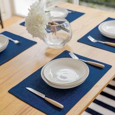 a wooden table topped with white plates and silverware next to a vase filled with flowers