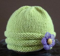 a green knitted hat with a flower on the front and side, sitting on top of a table