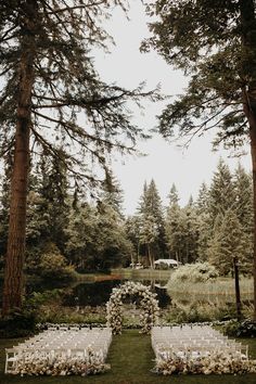 an outdoor ceremony set up in the woods with white chairs and flowers on each side