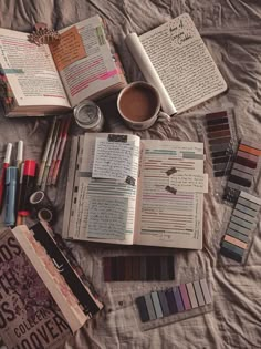 an open book sitting on top of a bed next to some pens and pencils