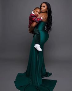 a woman in a green dress holding a baby and posing for the camera with her arms around