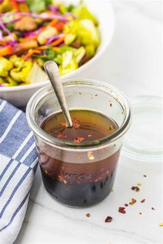 a bowl of salad with dressing in it next to a glass jar filled with dressing