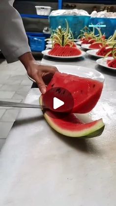 a person cutting up a piece of watermelon with a knife on a counter