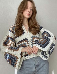 a woman wearing a crocheted sweater and jeans poses for the camera with her hands on her hips