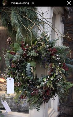 a wreath hanging on the front door of a house with evergreens, berries and pine cones