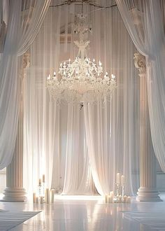 a chandelier hanging from the ceiling in front of white drapes and candles