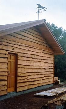 a wooden building with a weather vane on top of it's roof and windows