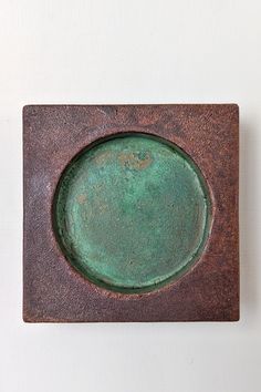 a green plate sitting on top of a brown square shaped object with rusted edges