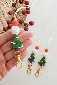 a hand holding three christmas tree shaped keychains with bells on them and two other ornaments in the background