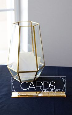 a glass vase sitting on top of a blue table cloth next to a card holder