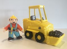 a toy man standing next to a yellow construction vehicle