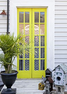 a yellow front door with birdhouses and houseplants on the porch next to it