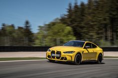 a yellow sports car driving on a road with trees in the backgrouund