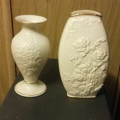 two white vases sitting next to each other on top of a black countertop