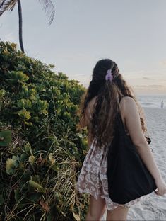 a woman walking on the beach carrying a black bag with a pink flower in her hair