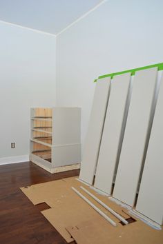 an empty room with white walls and wooden flooring being installed on the wall to create shelves