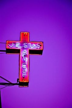 a neon sign that says jesus is alive on the side of a building in front of a purple sky