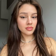 a woman with long brown hair wearing a choker and pearls on her neck is looking at the camera