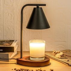 a candle and some books on a table next to a lamp that is turned on