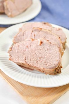 slices of meat sitting on top of a white plate next to a wooden cutting board