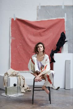 a woman is sitting on a chair in front of a red and white artwork piece