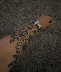 a person's arm with a flower tattoo on it and a cell phone in the other hand