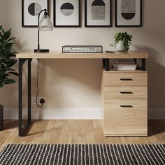 a wooden desk with three framed pictures on the wall above it and a plant next to it