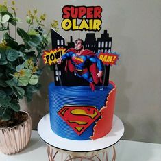 there is a superman cake on top of a table with flowers in the vase and a sign that says, super olair