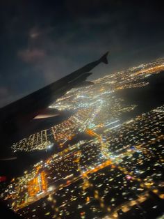 an airplane wing flying over a city at night with lights on the buildings and in the air