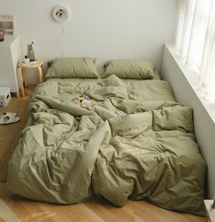 an unmade bed with green sheets and pillows in a room next to a window