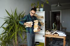 a man standing in front of a book shelf holding several stacks of books and looking at it