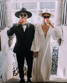 two people dressed in black and white are drinking beverages from their cups while standing on the steps