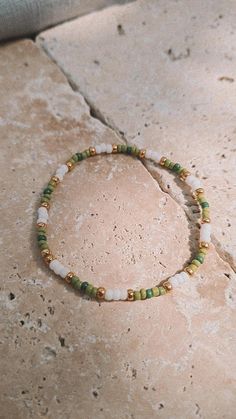 a green and white beaded bracelet sitting on top of a stone floor