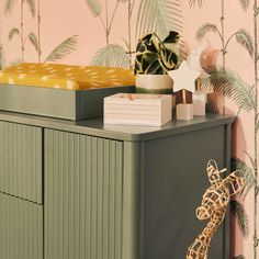 a giraffe figurine sitting on top of a dresser next to a plant