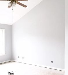 an empty room with a ceiling fan and white paint on the walls, in front of a window