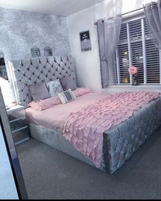 a large bed sitting in a bedroom next to a window covered in pink and silver sheets