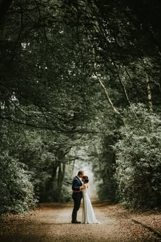 a bride and groom standing in the middle of a wooded path with trees on either side