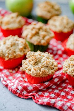 some muffins are sitting on a red and white checkered cloth with apples in the background