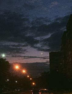 cars driving down the road at night with street lights and clouds in the sky behind them