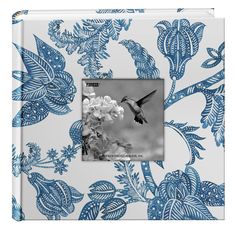 a blue and white flowered photo album with a hummingbird flying over it's head