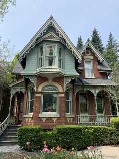 an old victorian style house with green trimmings and flowers in the front yard