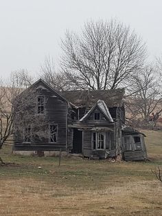 an old run down house sitting in the middle of a field with no leaves on it